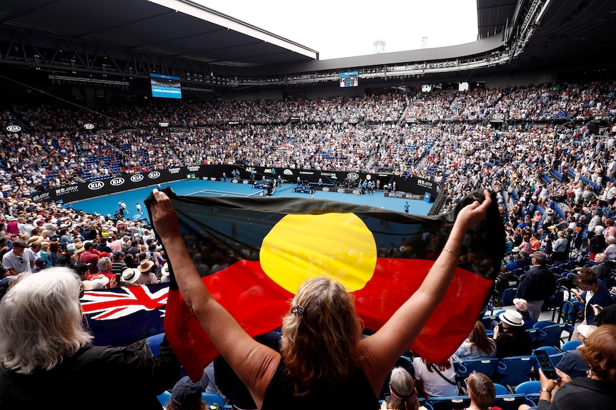 A woman holds up an Indigenous flag inside a tennis stadium