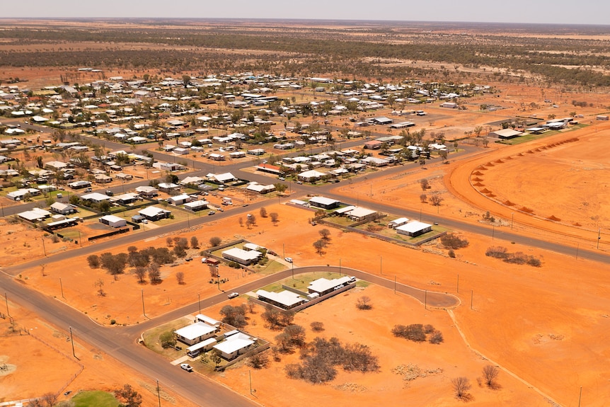 An aerial drone shot of an outback town with houses on rich, red dirt.