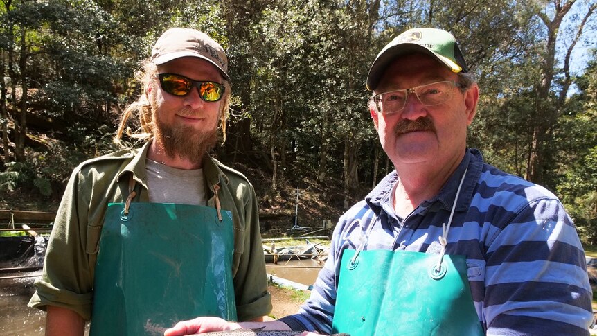 Roger and Russel Sydenham stand in green aprons holding a silver speckled trout.