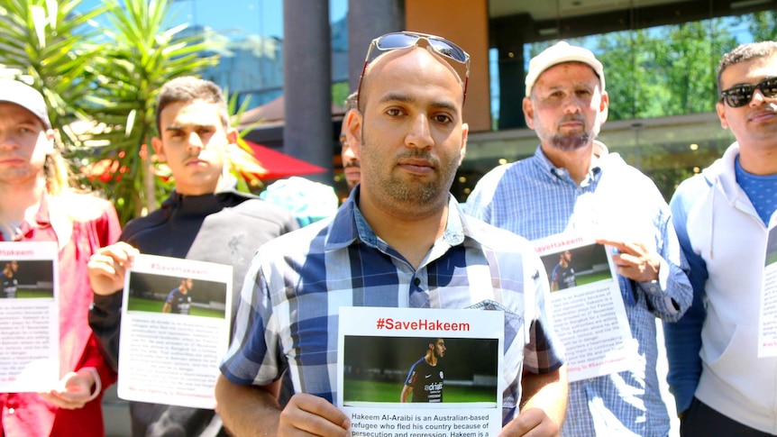 A group of seven campaigners holding #saveHakeem posters look to the camera during protest.