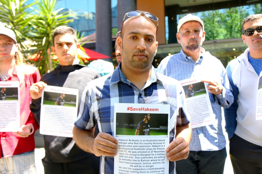 A group of seven campaigners holding #saveHakeem posters look to the camera during protest.