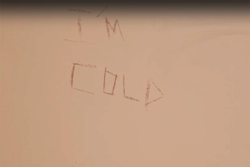 The words, “I’m cold, please help me God,” scrawled on the wall in a prison.