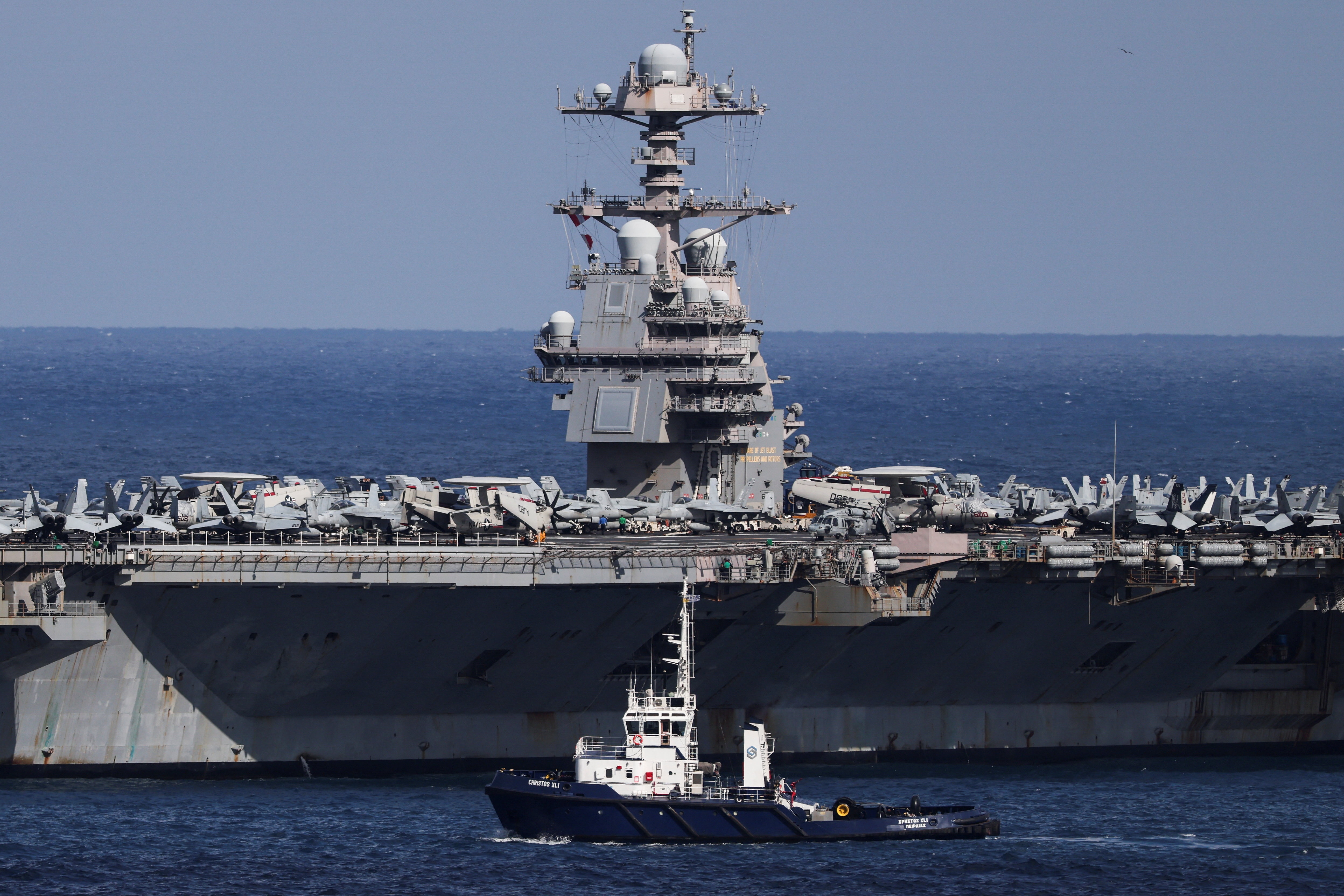 A large aircraft carrier is docked in the middle of the blue ocean, with a cloudless sky behind it