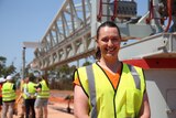 A woman with a brown ponytail wearing hi-vis smiles at a worksite