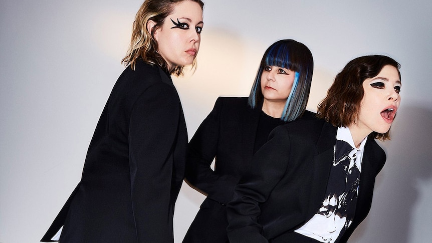 The three members of Sleater-Kinney wearing suits and heavy eye make-up