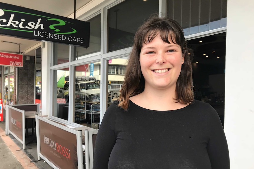 A young woman stands outside a cafe on a street.