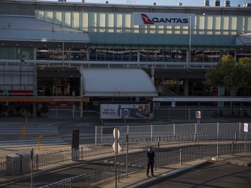 A security guard wearing a mask stands at a deserted Melbourne Airport in front of a Qantas sign