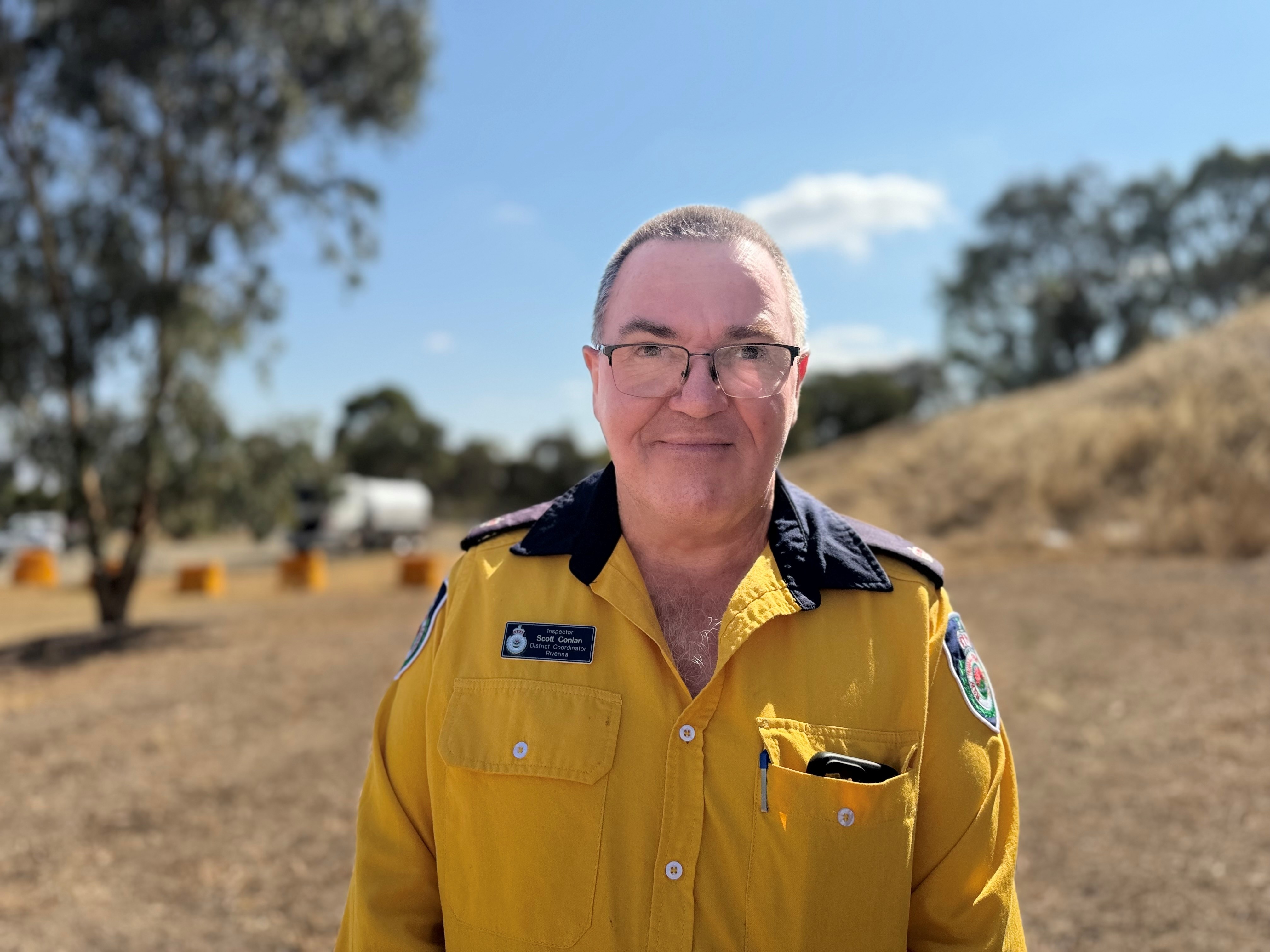 Retrato de um homem de óculos e camisa de trabalho amarela.