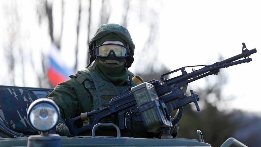 A military personnel member, believed to be a Russian serviceman, stands guard on a military vehicle