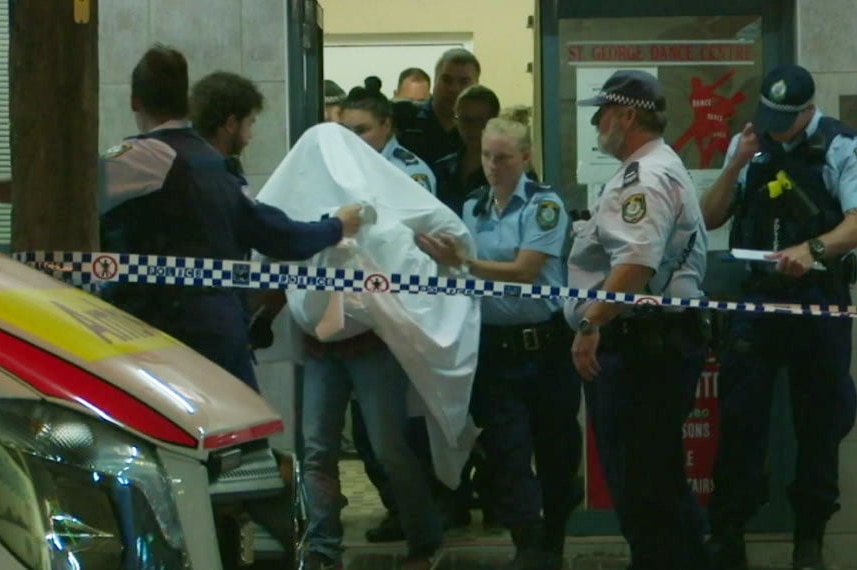 A man under a white blanket being led away by police