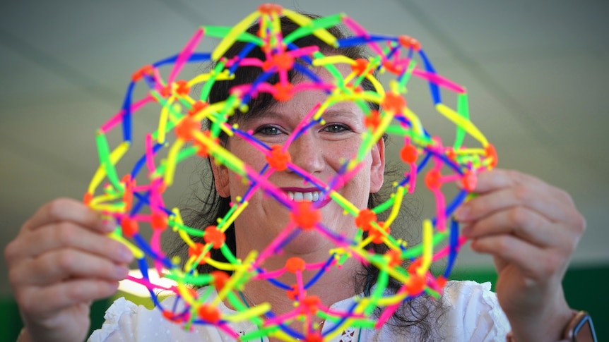A middle aged woman holding a colourful see through plastic toy in front of her face 