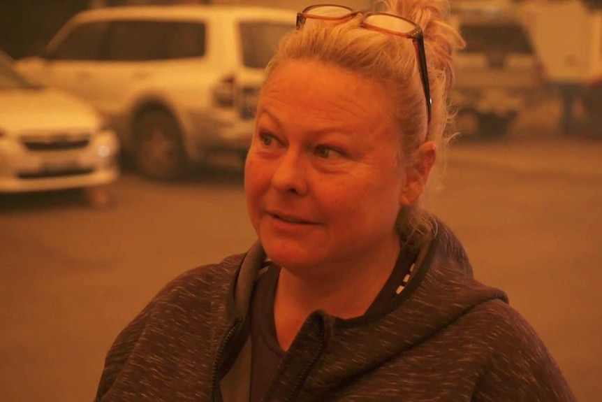 Evette Moroney stands in a car park at Eden, the light is orange from the smoke.