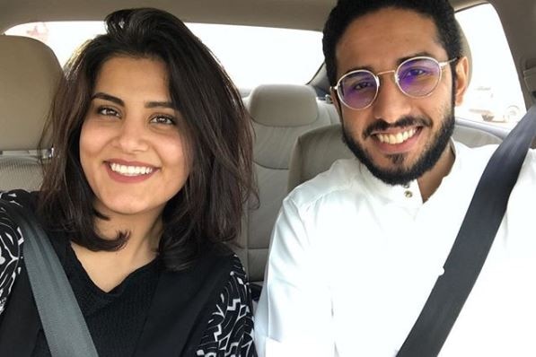 A woman and man pose in the front of a car for a selfie.
