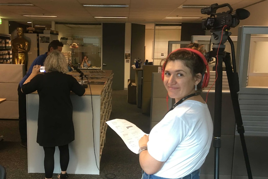 Anna Klauzner wearing red headphones standing next to camera as director sets up with Paul Barry.