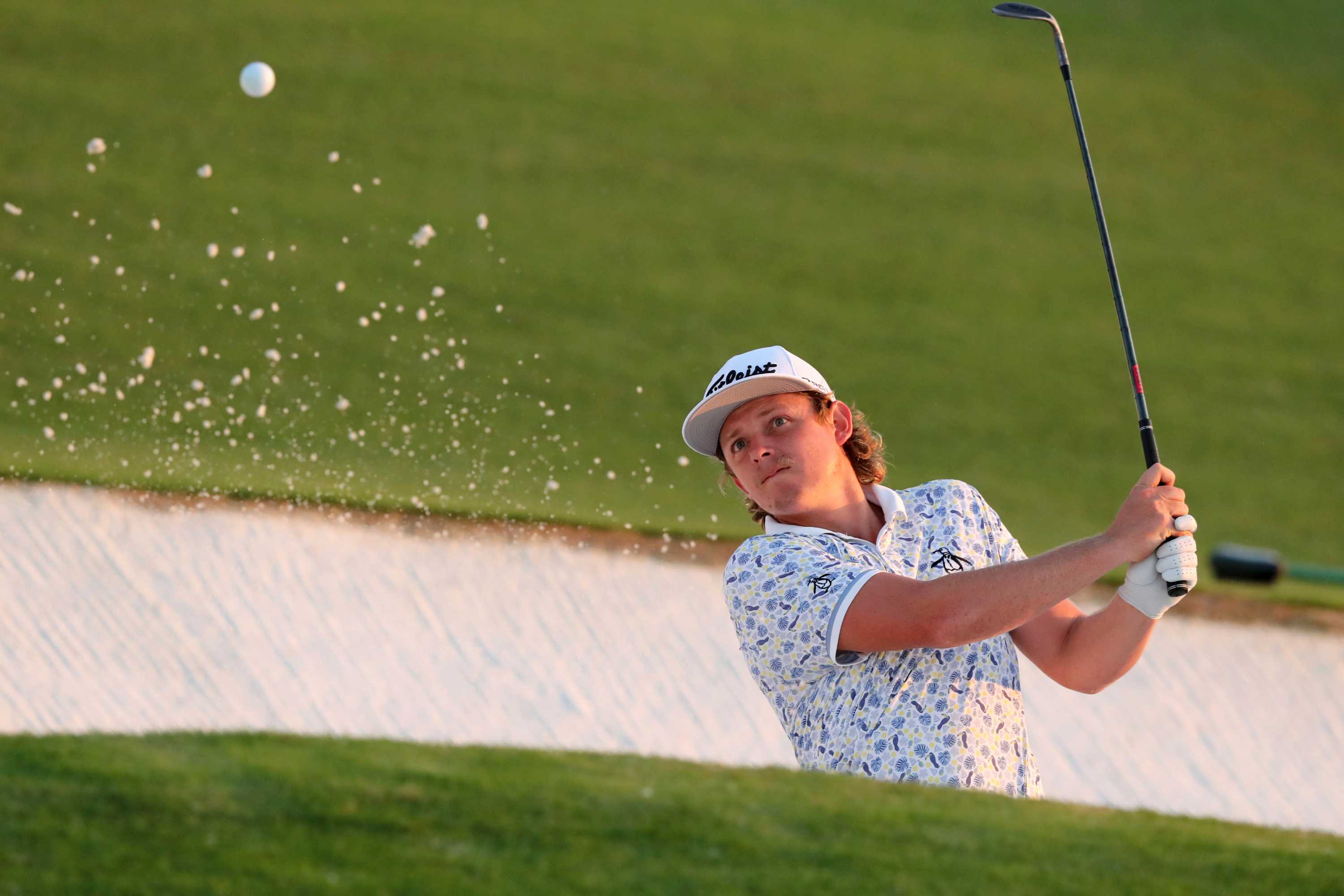 Cameron Smith watches as the ball flies out of the bunker, accompanied by some splashing sand