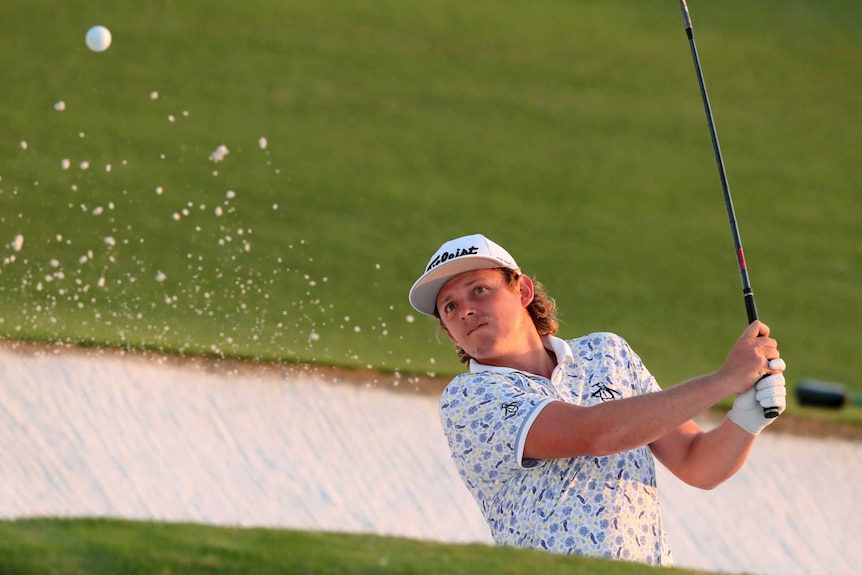 Cameron Smith watches as the ball flies out of the bunker, accompanied by some splashing sand