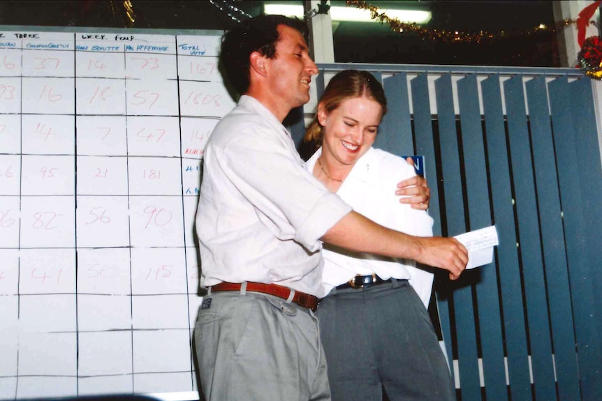 Photograph from the 1996 showing a man hugging his wife in front of an election tally board