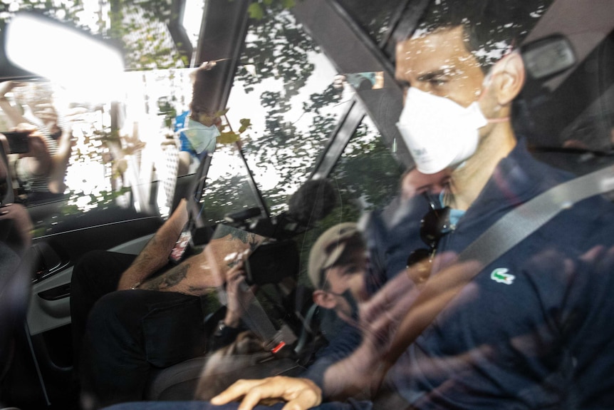 Serbian tennis player Novak Djokovic is seen through the window of a car with the reflection of photographers and journalists.