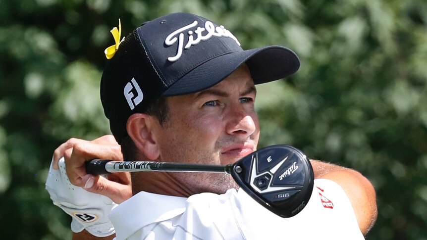 Adam Scott holds a pose after a shot, with a yellow ribbon on his hat.