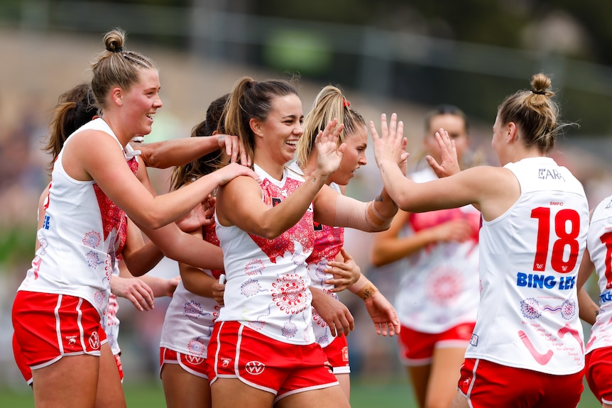 A group of Sydney Swans AFLW players surround a teammate to high-five her after a goal.