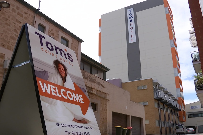 An a-frame sign points to the Tom's Court Hotel, a large white building with orange balconies