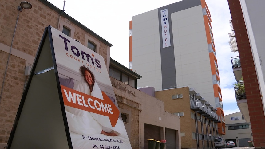 An a-frame sign points to the Tom's Court Hotel, a large white building with orange balconies