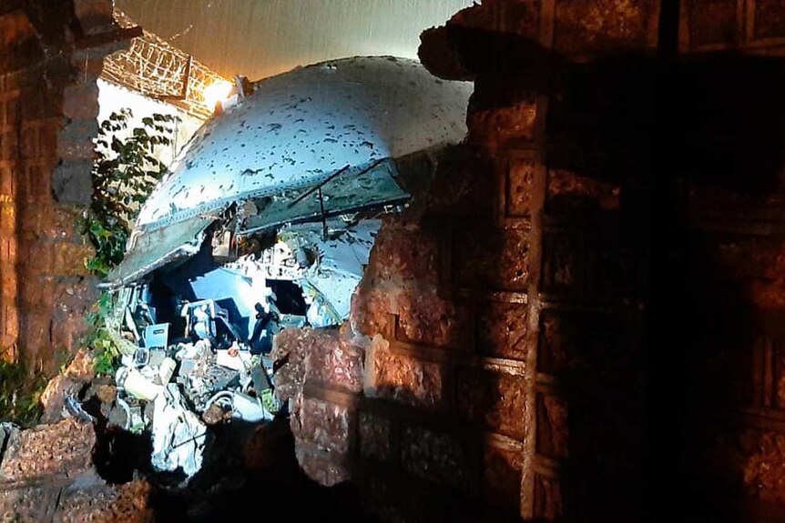 The wreckage of a plane pokes through a hole in a brick wall.