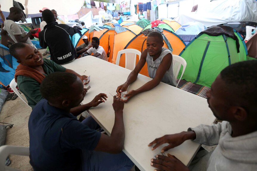 Four haitian migrants play cards at a table surrounded by tents in a shelter