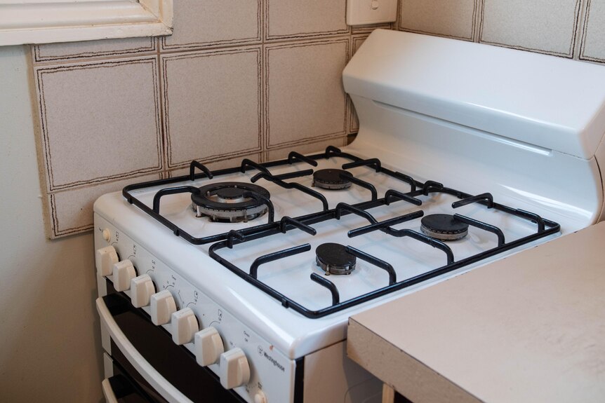 A gas stove top is seen up against a wall. It is white with black trim