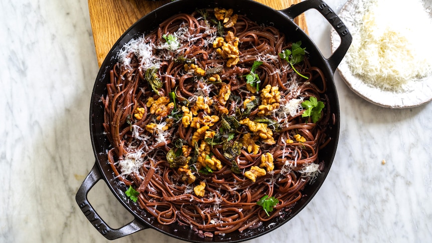 A wide pan filled with red wine pasta topped with sage, brown butter and walnuts, an easy vegetarian one pot meal.