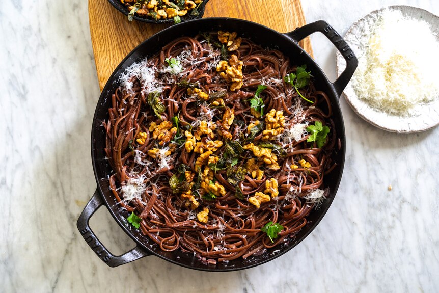 A wide pan filled with red wine pasta topped with sage, brown butter and walnuts, an easy vegetarian one pot meal.