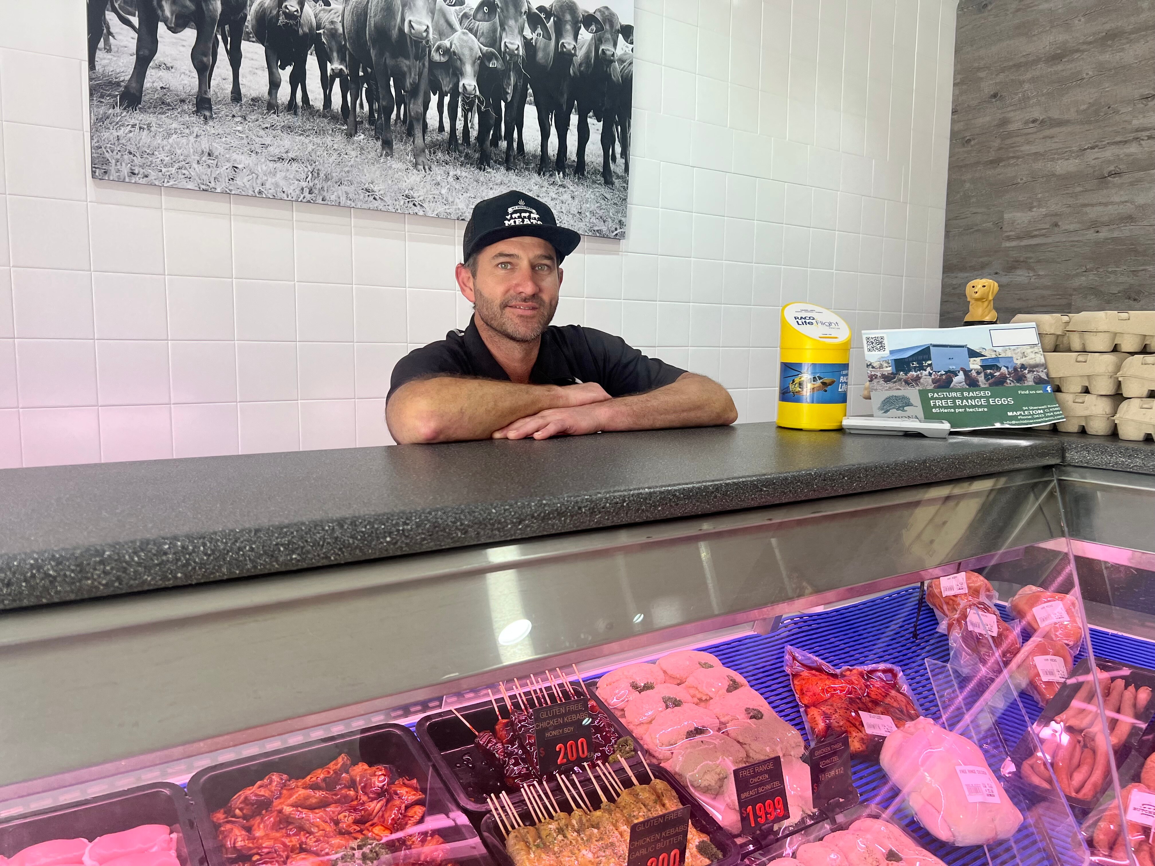 Man in black shirt standing at butcher shop counter.