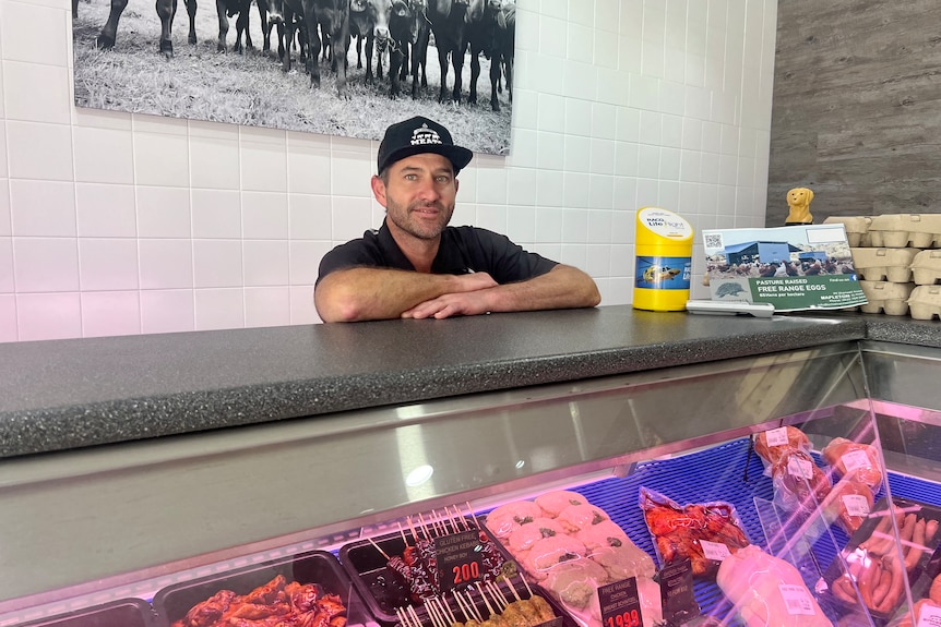 Man in black shirt standing at butcher shop counter.