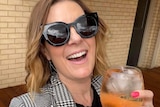 Woman smiling wearing sunglasses with a cocktail in hand. 