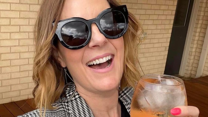 Woman smiling wearing sunglasses with a cocktail in hand. 