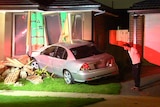 A car that has crashed through the side of a brick house.