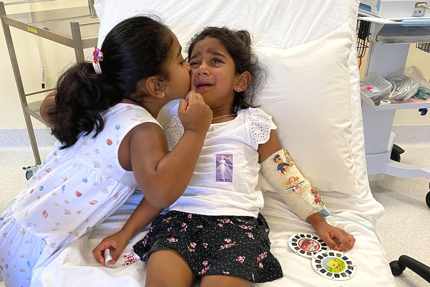 Tharnicaa comforted by sister Kopica in hospital on Christmas Island