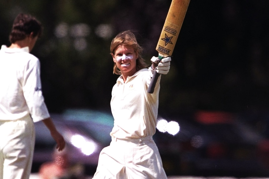 Joanne Broadbent smiles and holds her bat in the air.