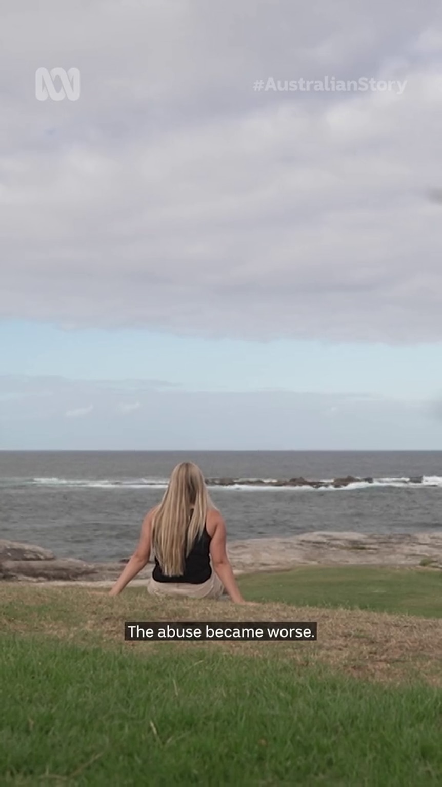 A young woman with blond hair looks out to the ocean as she sits on the grass