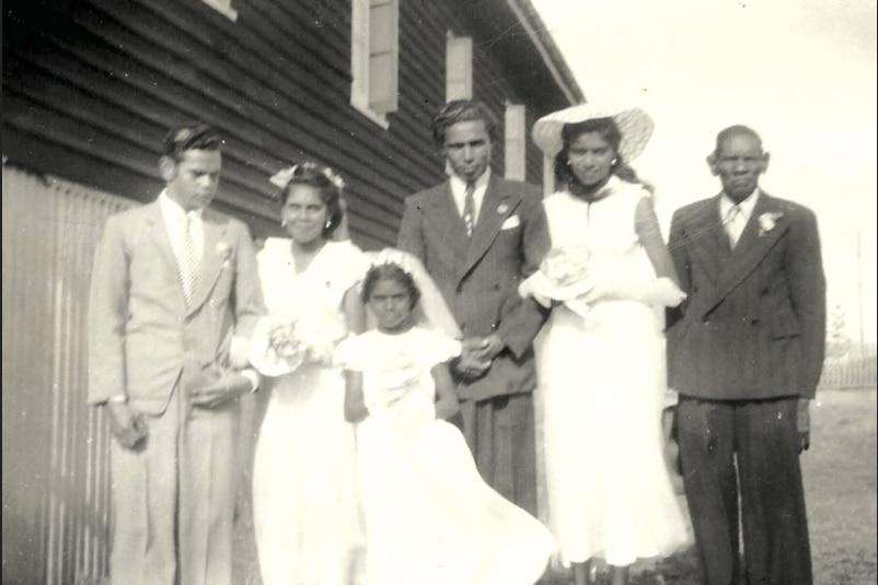 A wedding picture from the 1960s, with a couple, their bridal party and a little flower girl