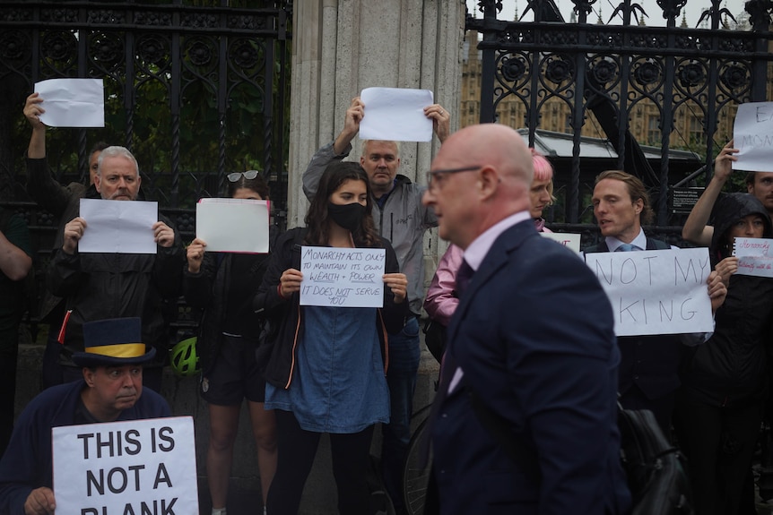 Protesters stand against the fence of parliament with blank A4 pages