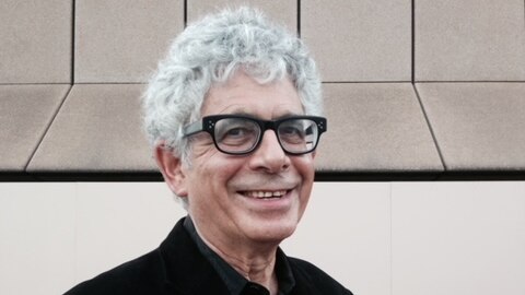 portrait of man in glasses, with curly white hair, wearing black suit and smiling 
