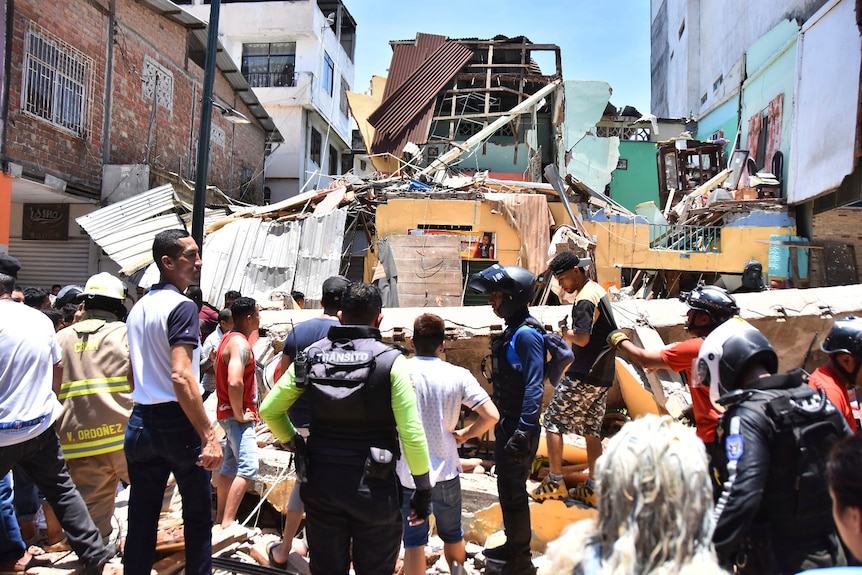 Residents and rescue workers stand in front of collapsed buildings.