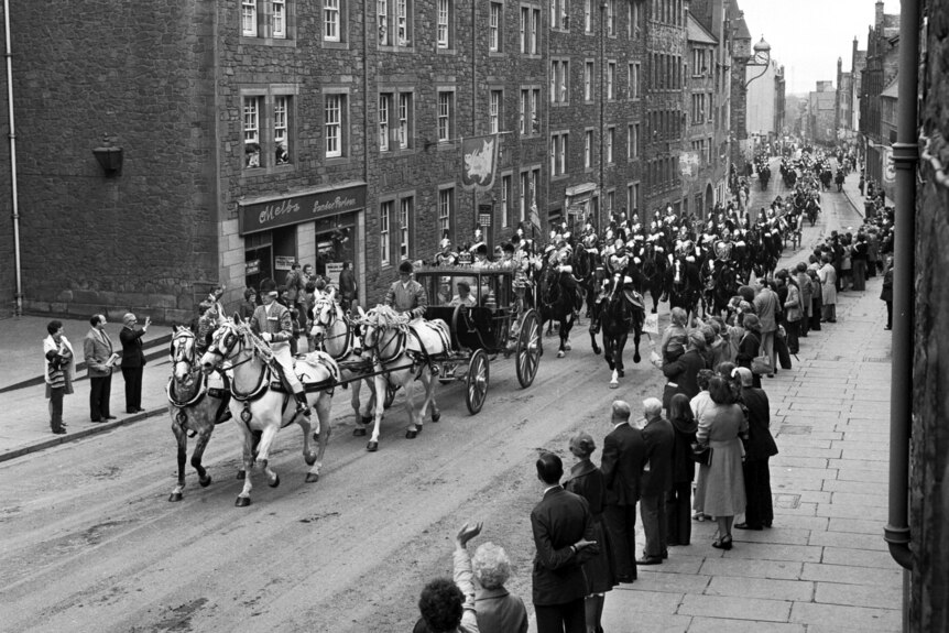 A black and white image of a crowd watching a horse-drawn carriage go by