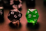 A close-up shot of to Dungeons and Dragos multi-sided dice, one black and one green, one a dark table