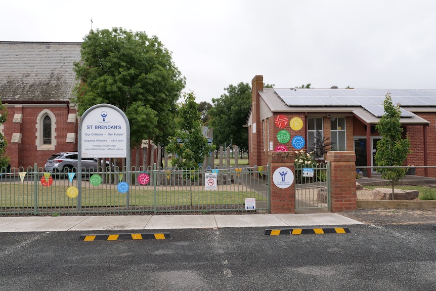 A brick school building behind a gate and a school sign