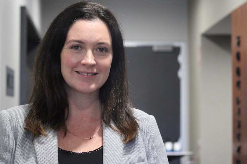 A dark haired woman inside, grey background.