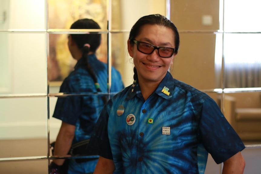 A young Asian man with platted hair, sunglasses and a bright blue shirt