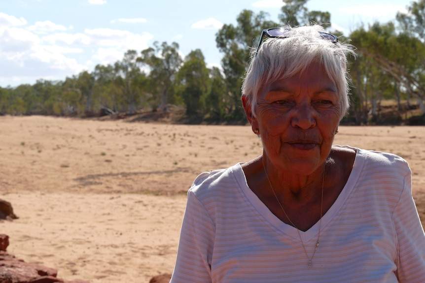 An older woman looks out at a dried up riverbed.