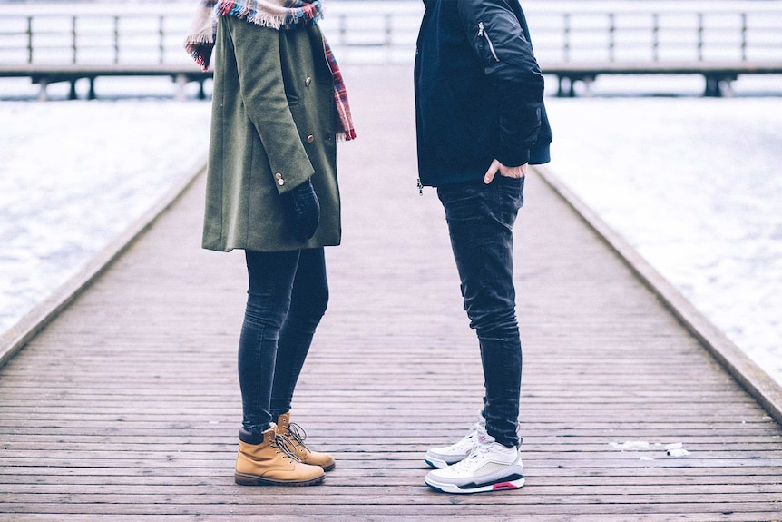 Couple standing slightly apart on a pier on an overcast day for a story about breaking up when the timing isn't right.